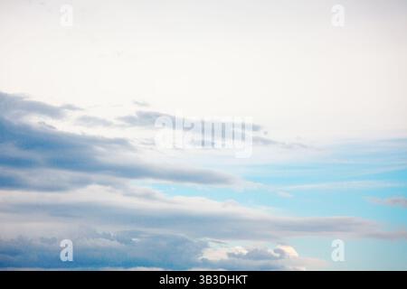 Serene sky with gentle gradient of colors transitioning from soft whites at the top to deep blues below. Wispy clouds stretch across the expanse, vary Stock Photo