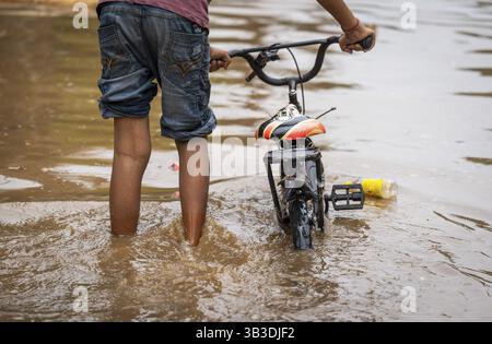 Children wade through a flooded street after heavy rains in Guwahati, India on April 28, 2025 Stock Photo