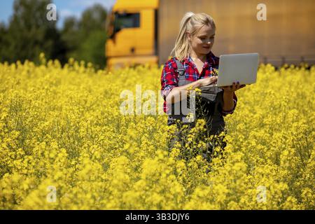 Eine Frau arbeitet an ihrem Laptop in einem leuchtenden Feld aus gelben Blumen, die Natur und Technik miteinander verbinden Stock Photo