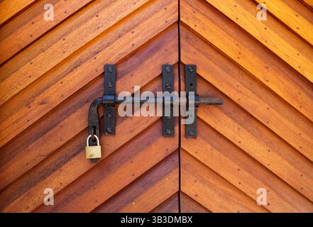 Close-up of a wooden door with diagonal chevron pattern, featuring a black metal latch and brass padlock. Stock Photo