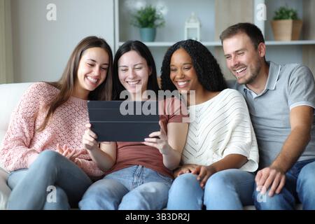 Happy interracial group of friends using tablet sitting on a couch at home Stock Photo