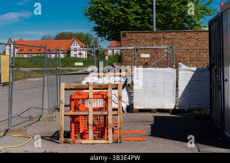 A construction site shows stacked materials and equipment enclosed by fencing. Bright weather highlights the surrounding buildings and greenery. The a Stock Photo