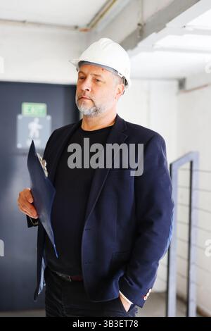Confident construction manager holding clipboard and inspecting site, low angle view Stock Photo