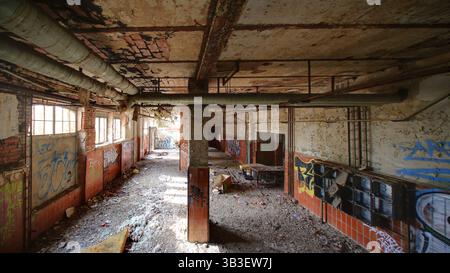 Graffiti filled hallway in a crumbling industrial building with broken tiles and debris. Stock Photo