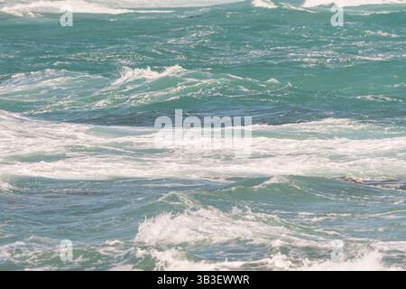 blue green sea water, small ocean waves topped by white foam close up showing turbulence or movement concept abstract nature background, backdrop Stock Photo