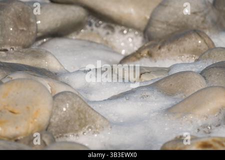 rocks, stones, pebbles close up, shiny and wet surrounded by sea water and foam concept abstract nature background, backdrop, wallpaper Stock Photo