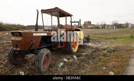 Villanova del ghebbo, italy 2 april 2025: an old. Rusty same tractor with a yellow tank sits parked in a muddy field near the town of villanova del gh Stock Photo