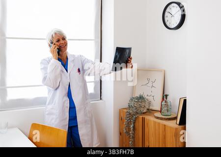 Senior female doctor examining medical X-ray standing at desk in hospital Stock Photo