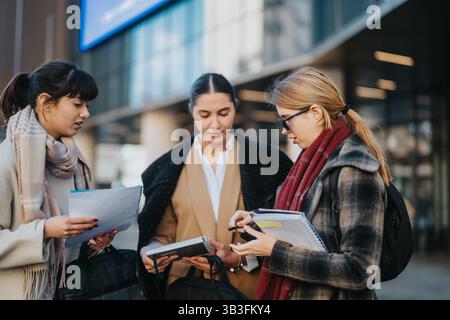 Three businesswomen collaborating outdoors with notepads and documents in hand Stock Photo