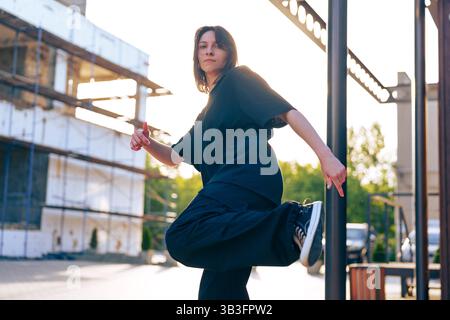 Dancer performs expressive movement outdoors in urban setting during golden hour Stock Photo
