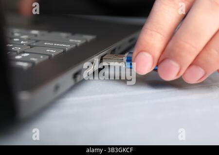 Woman inserting flash drive into laptop at gray table, closeup Stock Photo
