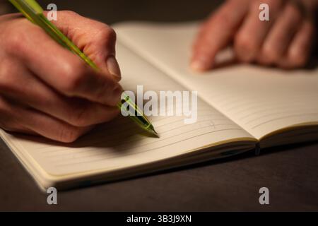 Close up image of human holding pen and writing something on blank white page in notebook Stock Photo