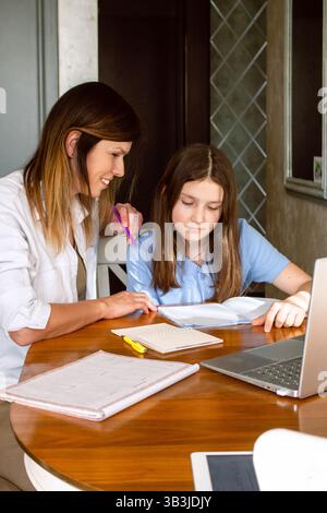 Preteen girl doing homework with mom at home. Mother explaining difficult school subject to her daughter. Spending quality time with child. Happy fami Stock Photo