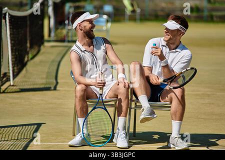 Two friends relax with smiles on their faces while taking a break from summer tennis. Stock Photo
