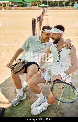 Two men enjoy each others company while resting on the tennis court during summer. Stock Photo