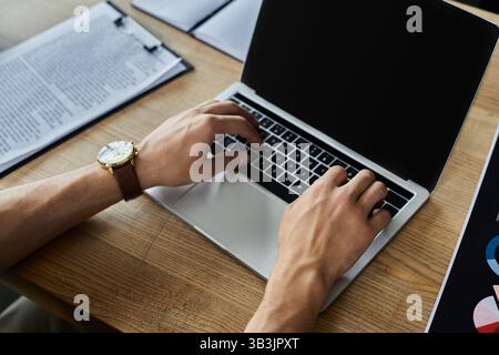 Hands type diligently on a laptop while organized paperwork rests nearby during busy office hours. Stock Photo