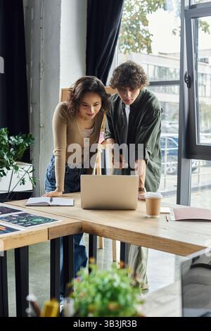 Two colleagues engage in a focused discussion while reviewing digital content at their workspace. Stock Photo