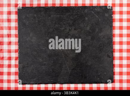 Top view of an empty dark cutting board on checkered red tablecloth, perfect for food presentation or background Stock Photo
