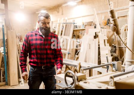 Skilled carpenter working in a workshop surrounded by wood and tools during the day Stock Photo