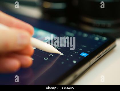 Close-up person using digital stylus tablet screen adjust image parameters photo editing software, likely Lightroom. Interface shows sliders editing e Stock Photo