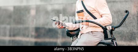 Young man enjoying coffee while checking tablet on bike in urban setting Stock Photo