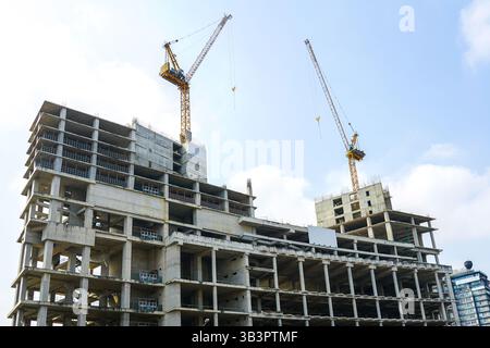 Construction of a new reinforced concrete high-rise building, unfinished building frame with two tall tower jib cranes against the sky background Stock Photo
