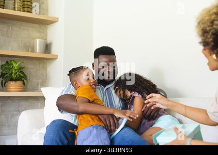Diverse family reading together in living room on white sofa, with tablet and gift box Stock Photo