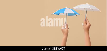 Hands holding small umbrellas on beige background with space for text Stock Photo