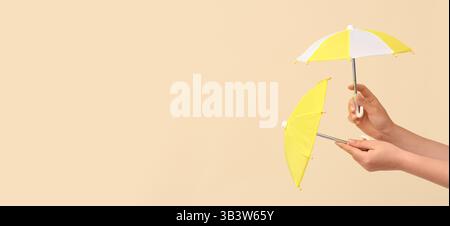 Hands holding small umbrellas on beige background with space for text Stock Photo