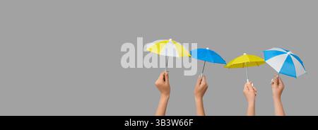 Hands holding small umbrellas on grey background with space for text Stock Photo