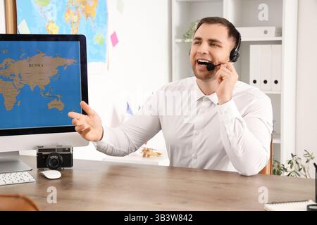Male travel agent with headset working at table in office Stock Photo