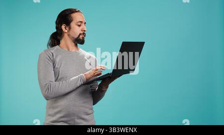 Portrait of smiling person spending time on laptop, isolated over studio background. Cheerful man checking social media posts on notebook, enjoying leisure time, camera B Stock Photo