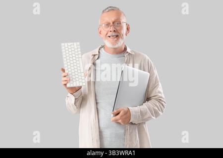 Mature programmer with laptop and computer keyboard on light background Stock Photo
