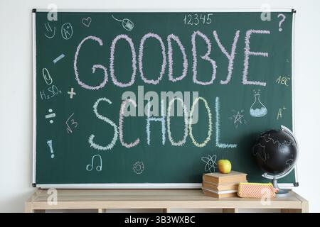 Globe with books and text GOODBYE SCHOOL on blackboard in classroom Stock Photo