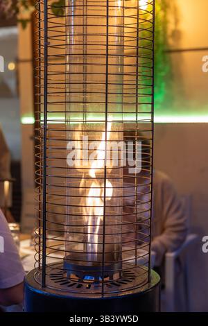 In a lively urban setting, diners enjoy their meals bathed in the glow of a modern flame heater, creating a welcoming ambiance on a crisp evening unde Stock Photo