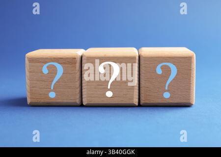 Wooden cubes with question marks on blue background, closeup Stock Photo