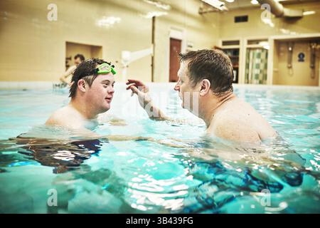 Pool, disability and down syndrome man in swimming class for exercise, mental and physical development in water. Fitness, workout and disabled person Stock Photo