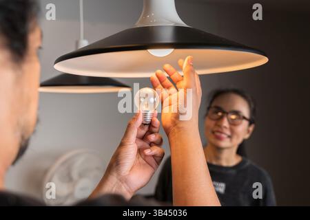 Male hands compare an incandescent light bulb and a LED lamp. Changing Light Bulb. Man installs light fixture in new home. A man changes a light bulb Stock Photo