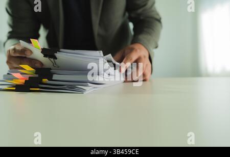 Stacks of paper files and checking document businessman checks financial documents on his laptop, managing corporate reports and legal paperwork at hi Stock Photo
