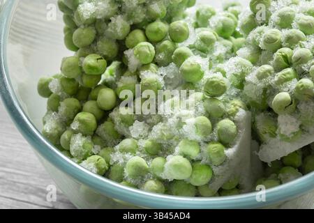 Frozen garden peas defrosting in a glass bowl. On a grey wood background. Stock Photo