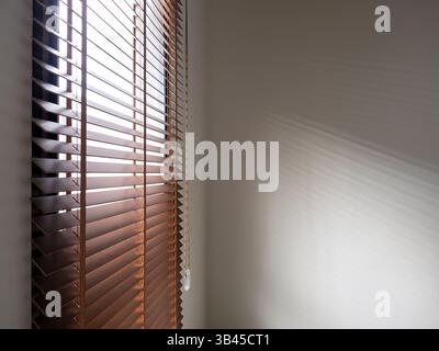 Image of brown wooden window blinds ropes being pulled open to allow sunlight into the room, casting light and shadow, overlay patterns on empty blank Stock Photo