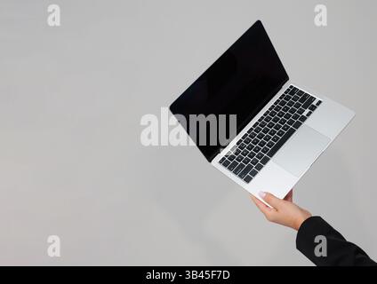 Female hand holding open laptop computer with black screen on grey background, minimal tech business concept. Stock Photo