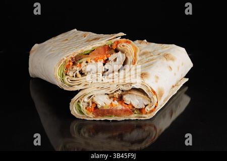 Freshly made chicken shawarma wrap cut in half, filled with grilled chicken, vegetables, and sauce, isolated on black. Stock Photo