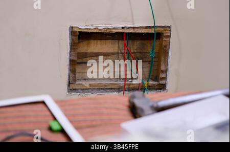 Electrician working on exposed wiring in a wall during renovation process. Tools and materials are scattered nearby. Stock Photo