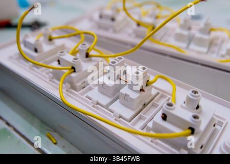 Electric wires are being connected to white terminal blocks in a workshop setting. Stock Photo
