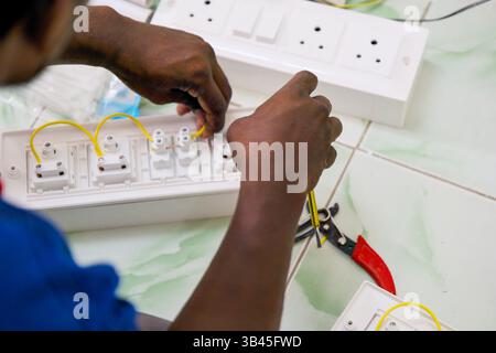 Hands carefully connect wires to power sockets on a clean workspace during electrical installation. Stock Photo