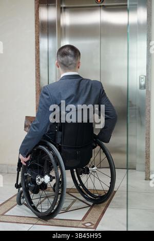 Disabled man in wheelchair waiting for elevator inside office building Stock Photo