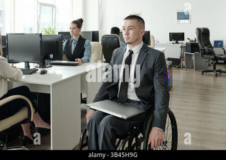 Disabled businessman with laptop on his knees moving along open space office Stock Photo
