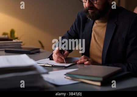 Cropped shot of mature male counselor in smart casual attire analyzing symptoms of patient and taking notes on paper document Stock Photo