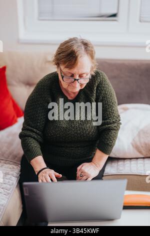 Elderly woman using a laptop seated on a comfortable couch in a cozy home Stock Photo